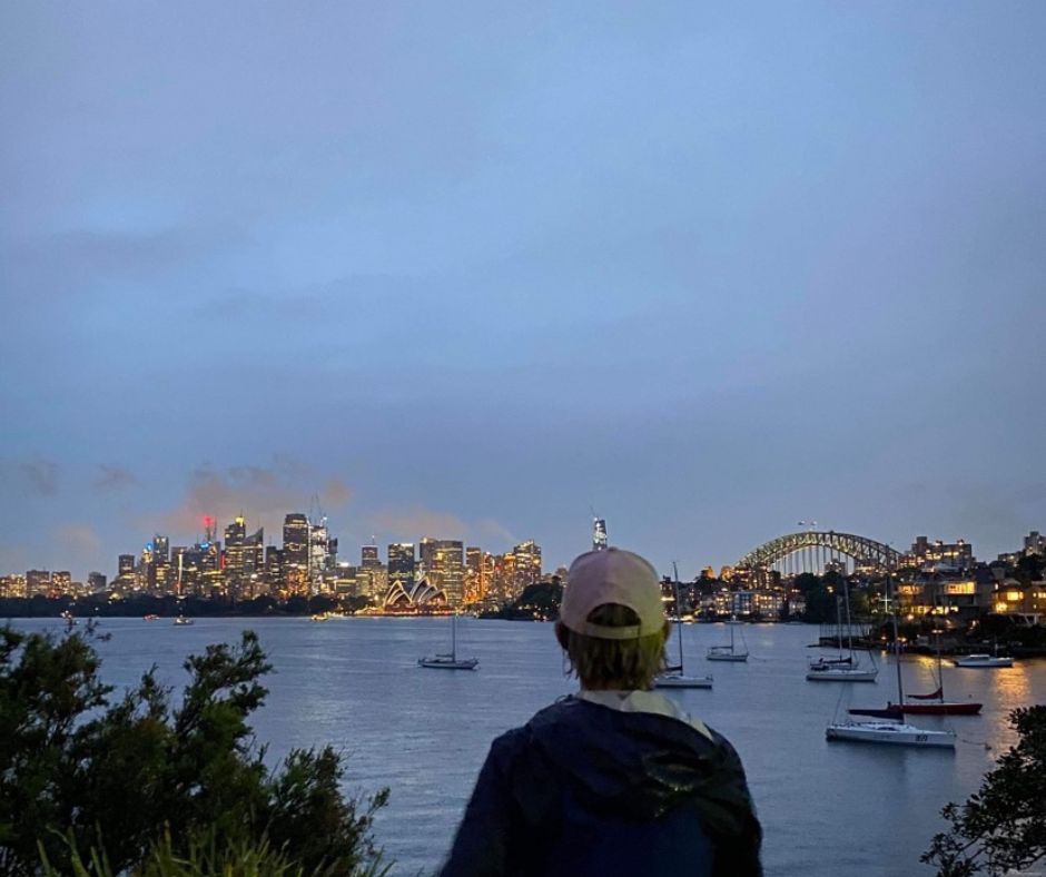Back view of person in cap looking at the skyline of Sydney at dusk