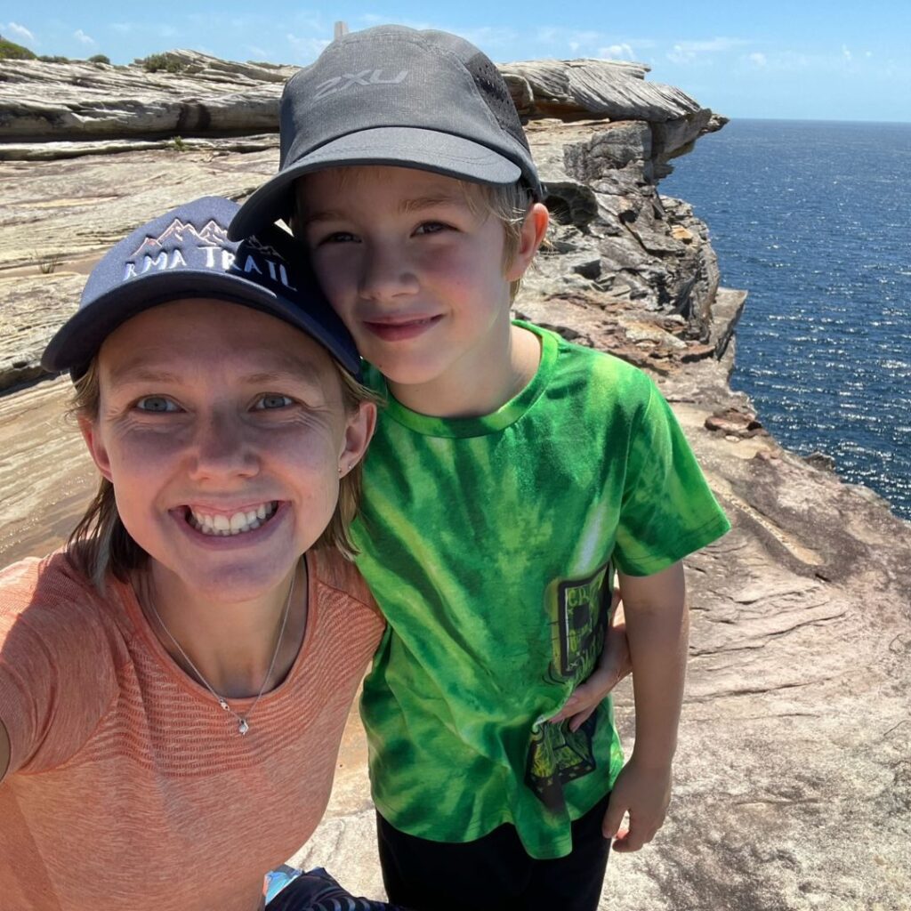 Lexy Wilson smiling with child in front of coastal rocks