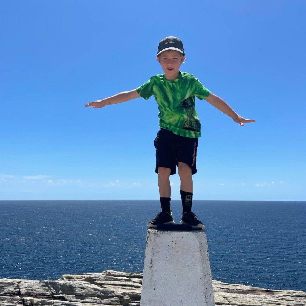 Child balancing on concrete bollard with sea in the background